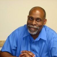 Image of a male in a collared blue shirt smiling.